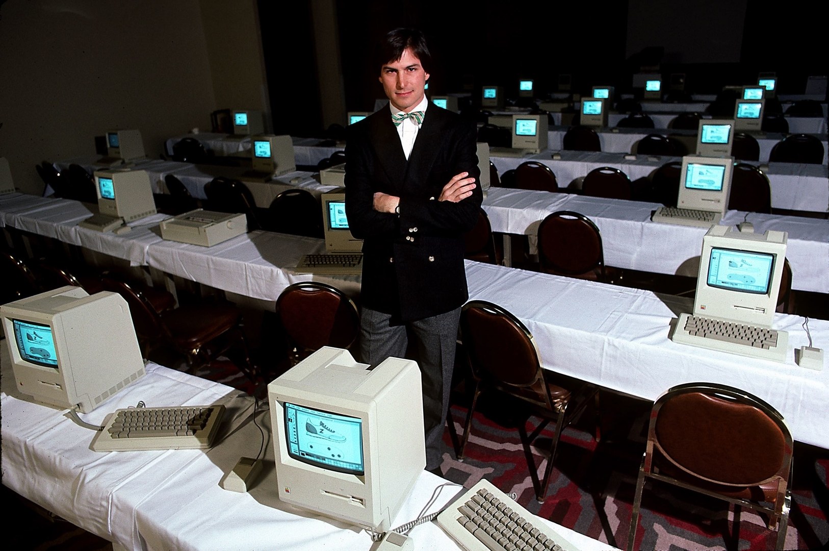 A young Steve Jobs in front of first generation Macintosh computers